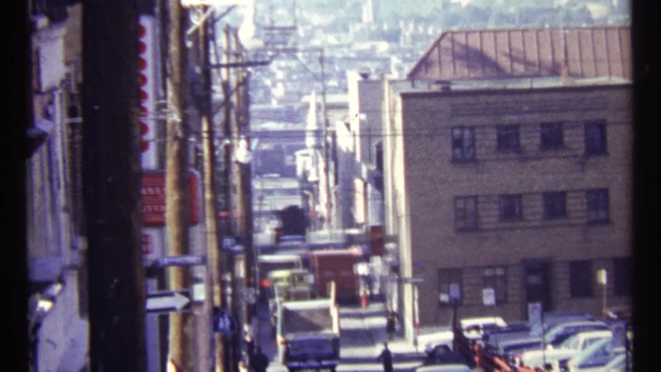 1967 Ottawa frame showing a narrow downhill street with vehicles, pedestrians, a small storefront sign, and mid-century building facades.