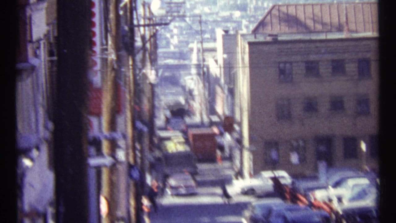 Soft, handheld 1967 Ottawa street frame showing traffic, building fronts, and poles in bright daylight.