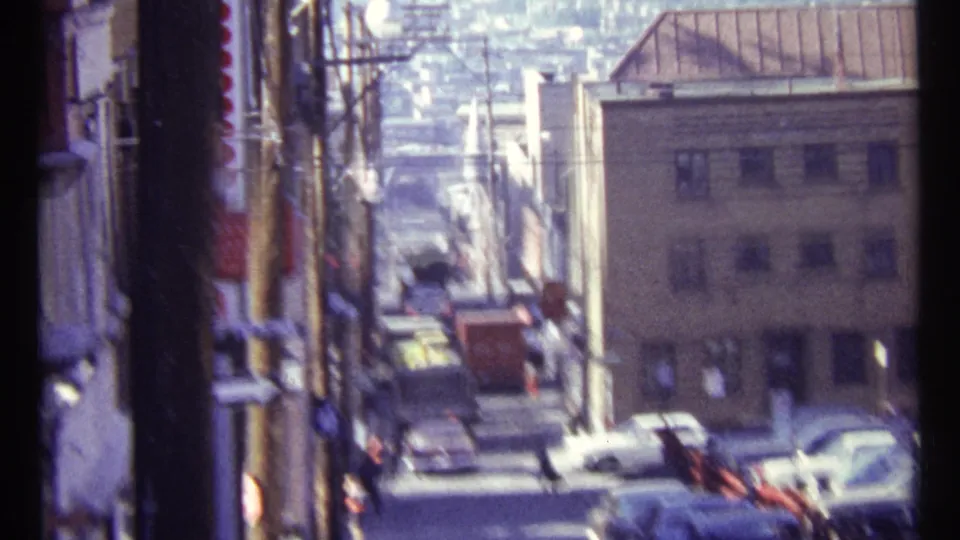 Soft, handheld 1967 Ottawa street frame showing traffic, building fronts, and poles in bright daylight.