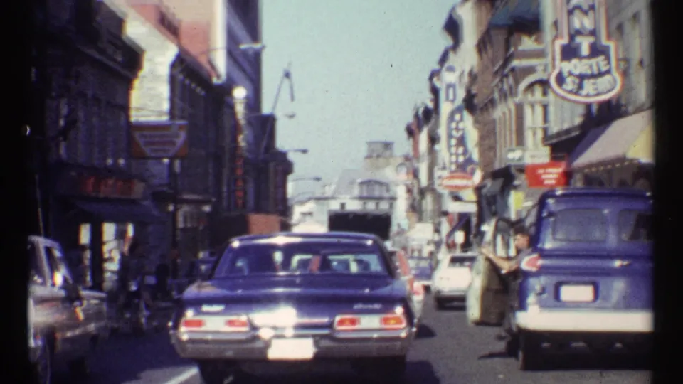 1967 Ottawa street traffic with mid-century cars, storefront signs, and pedestrians near a blue van.