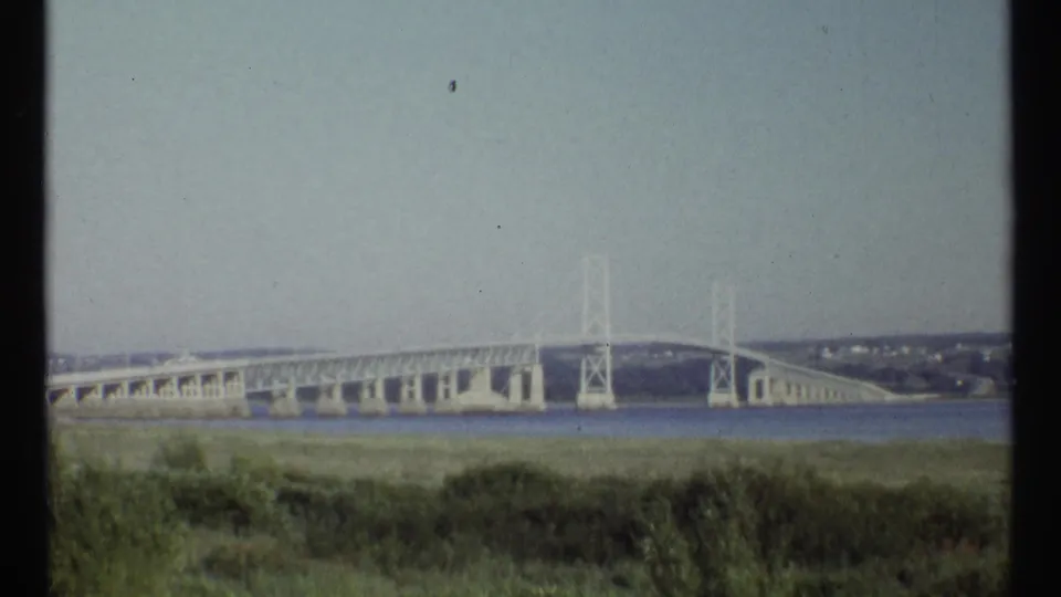 Distant 1967 Ottawa bridge view with white towers, roadway span, water, and soft 8mm color fading.
