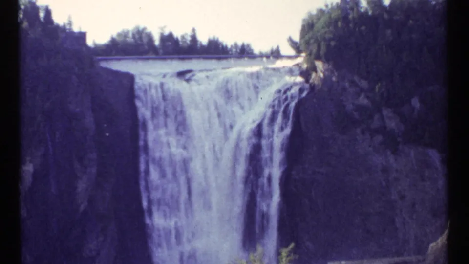 1967 Ottawa 8mm frame showing a waterfall spilling over a broad ledge into a rocky gorge with trees above.