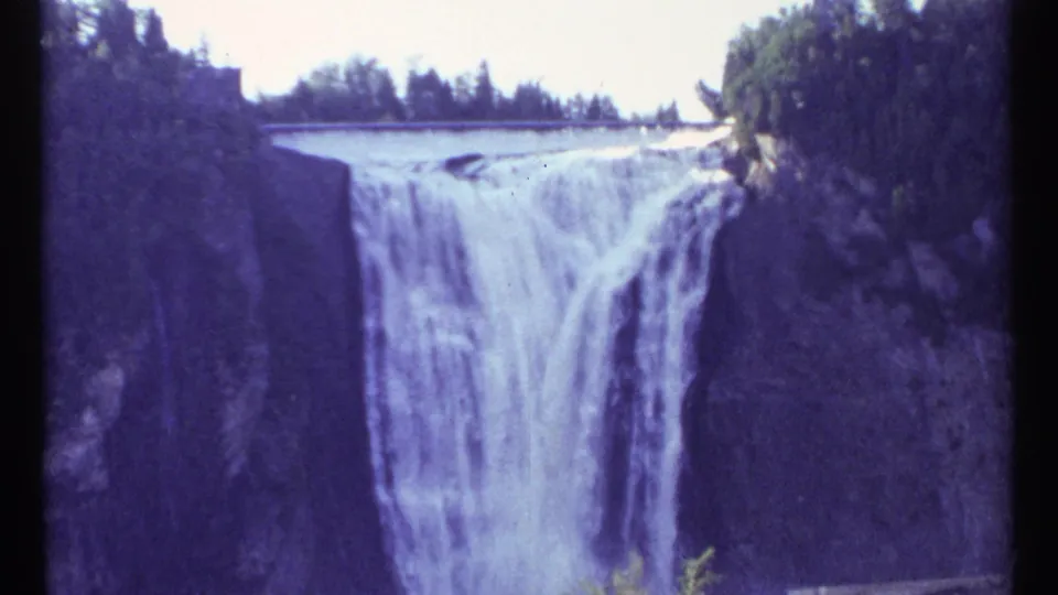 1967 8mm Ottawa-area view of a broad waterfall cascading between dark rock walls with trees along the rim.