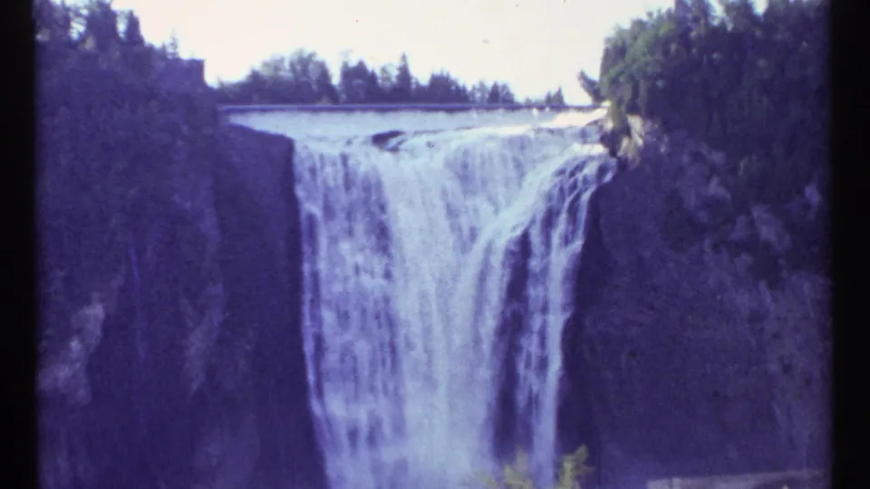 1967 8mm frame from Ottawa, Canada, showing heavy water flow over a wide ledge bordered by trees and rock.