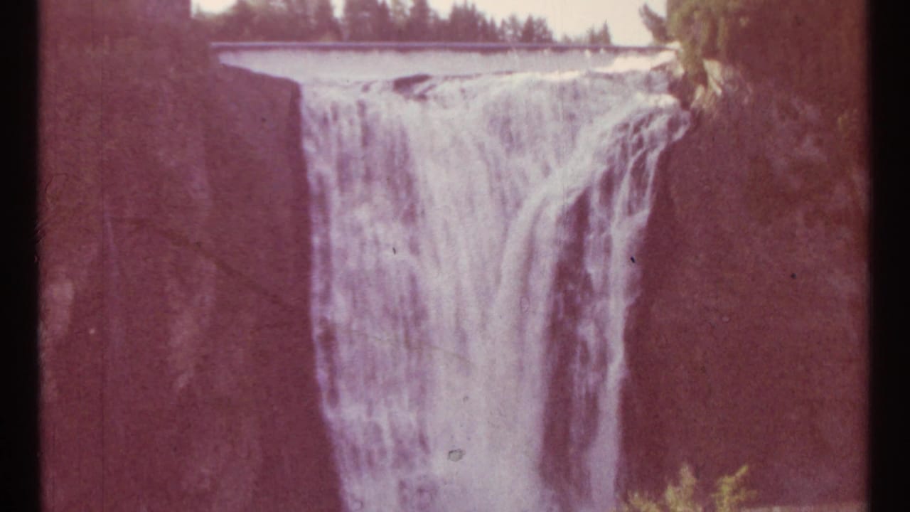 Waterfall dropping over rocky cliffs with trees along the rim.