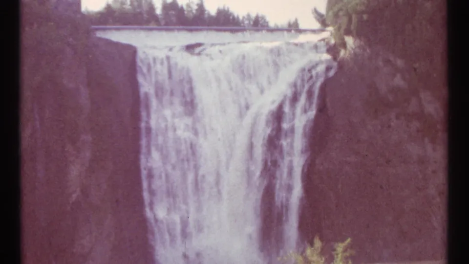 1967 Ottawa 8mm frame of a wide waterfall viewed across a gorge, with dark rock faces and trees at the rim.