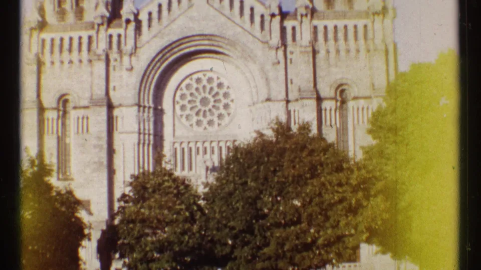 1967 Ottawa home-movie frame showing a stone church exterior with a large rose window partly obscured by trees.