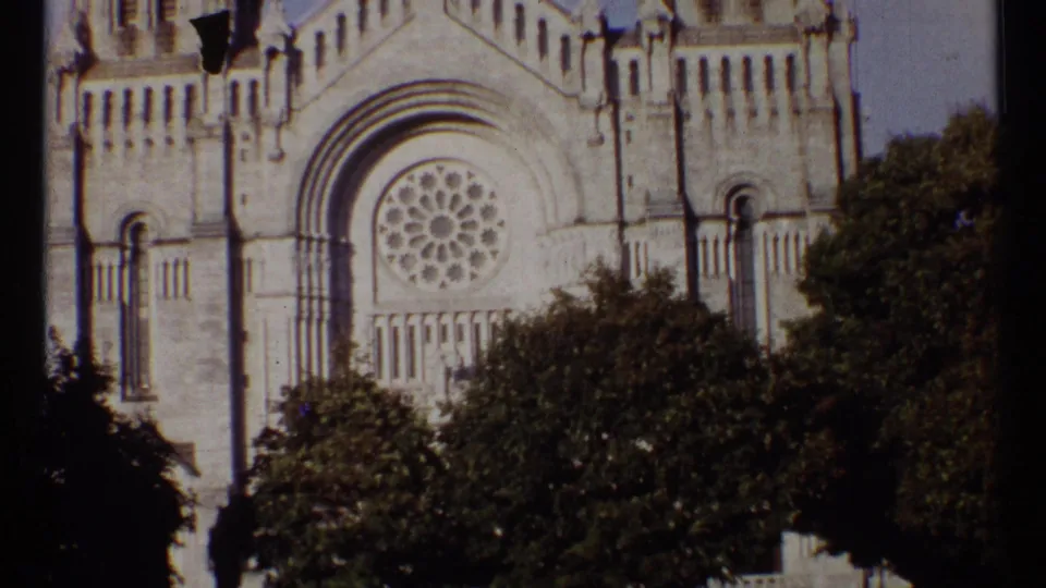 1967 Ottawa 8mm frame of a church facade with a rose window, arched doorway, and dark trees in front.