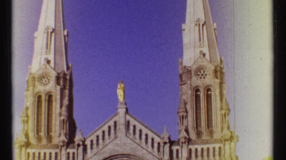 1967 Ottawa 8mm frame showing Notre Dame Cathedral's twin spires, central roofline statue, and blue sky.