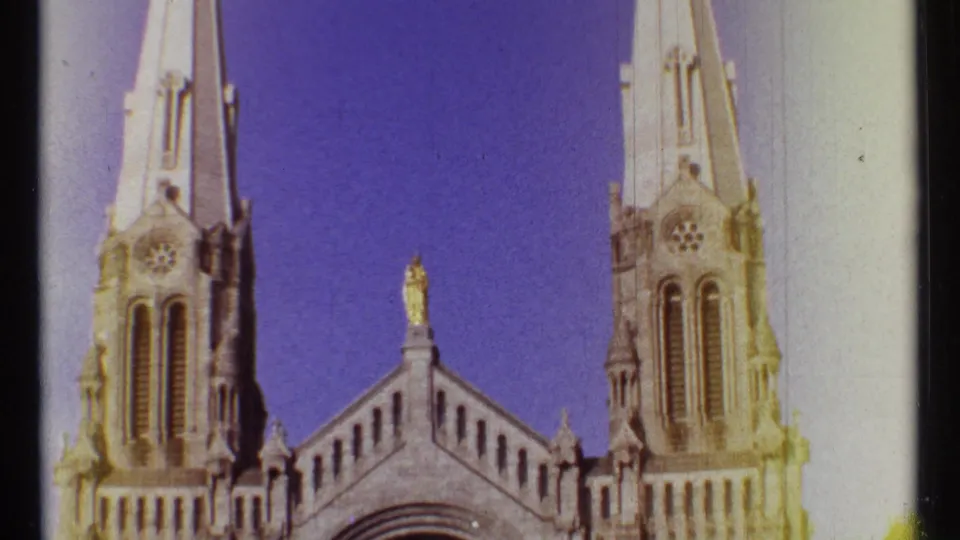 1967 Ottawa 8mm frame with Notre Dame Cathedral's twin spires, roofline statue, and stone details against a clear blue sky.
