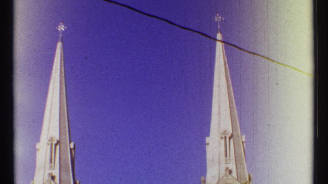 Two pointed church spires with crosses against a purple-blue sky and a dark overhead line.