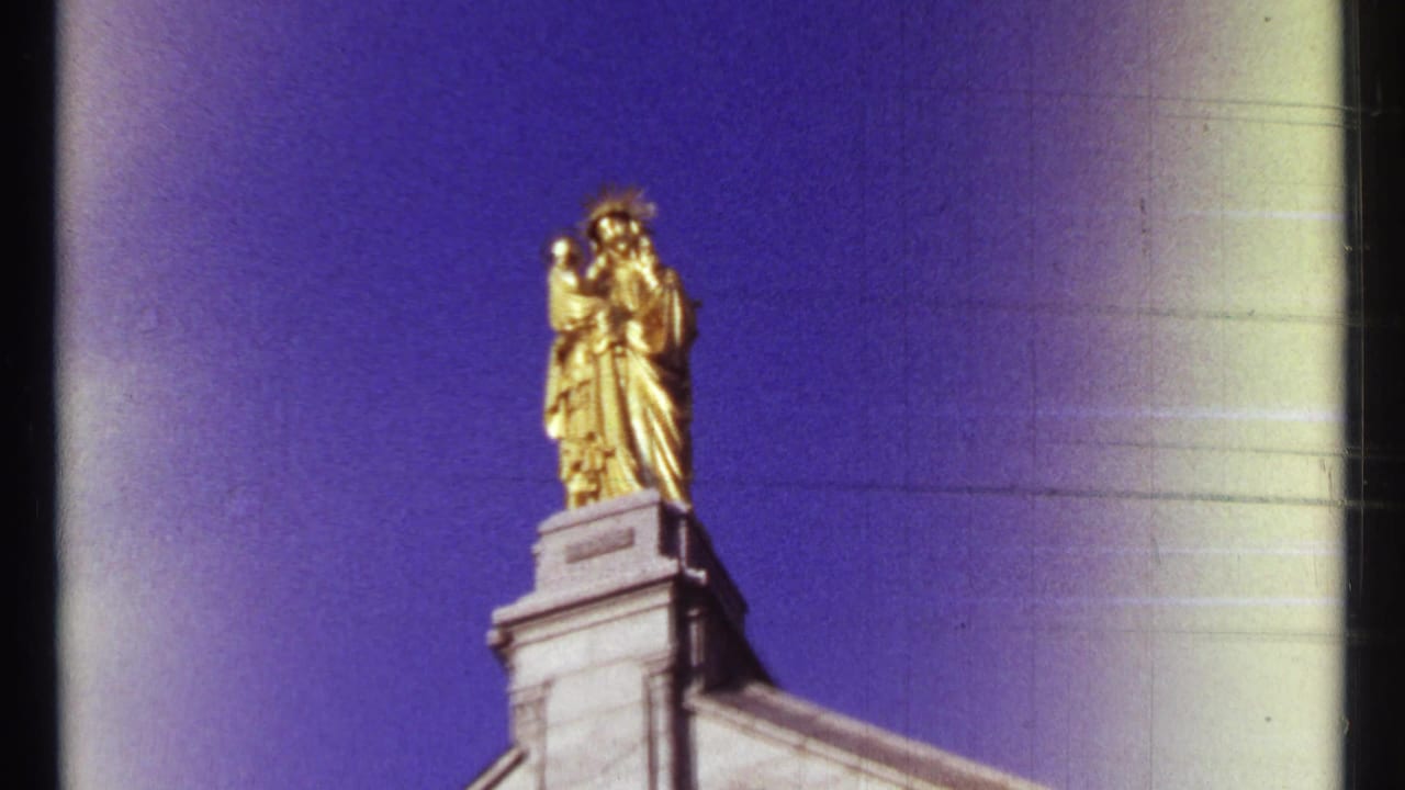 Golden religious statue atop a stone building against a blue sky.