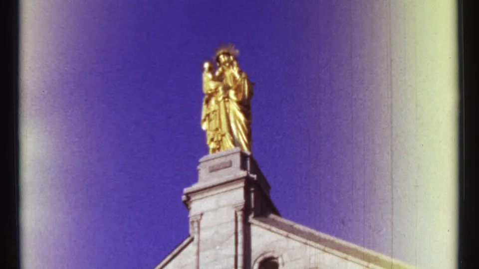 Low-angle 1967 Ottawa view of a golden religious statue on a stone structure, framed by blue sky and visible film gate edges.
