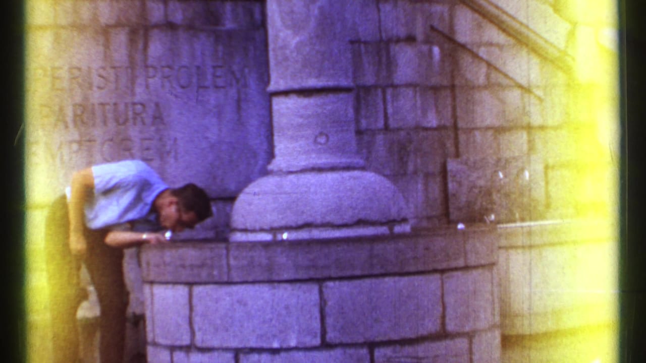 The man remains bent over the stone fountain in Ottawa, with engraved wall lettering and a column base behind him.