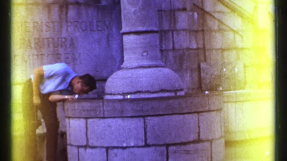 A low, handheld 8mm view shows the man still leaning into the Ottawa stone fountain beneath partially visible engraved text.