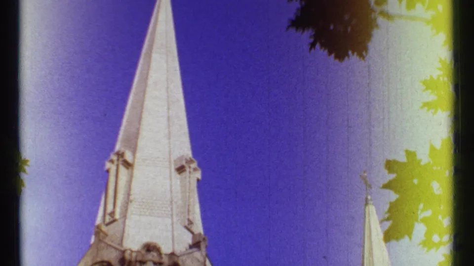 1967 Ottawa home-movie frame showing the church steeple cropped low, with foliage silhouettes and strong edge exposure flare.