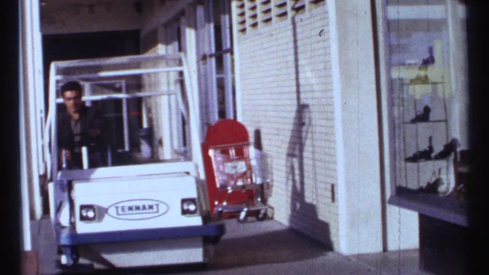 In Ottawa 1967 footage, a man drives a white Tennant-branded cart beside shop windows and a red cart on the sidewalk.