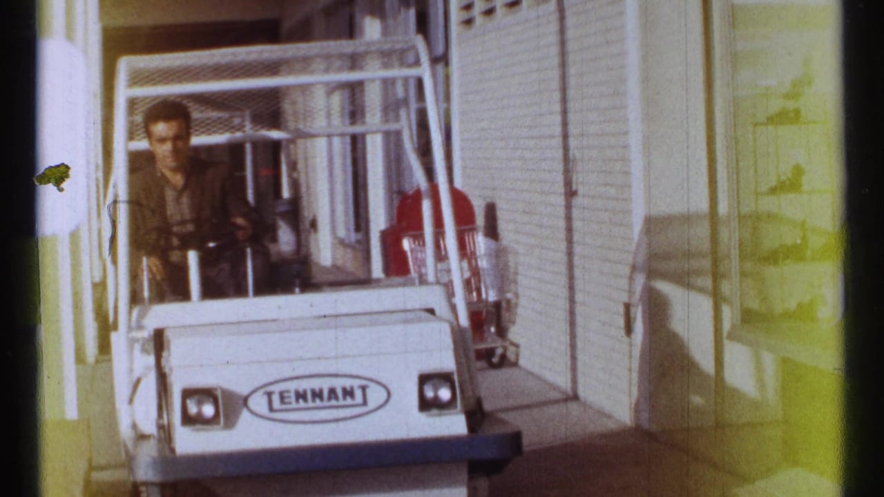 White Tennant cart approaching along a sidewalk beside shop windows and a red cart.