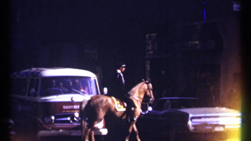 1967 Ottawa street scene with a mounted police officer riding near period cars and a red and white van under dark storefronts.