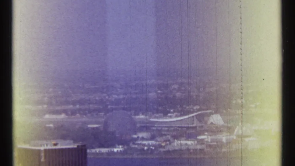 1967 Ottawa frame with a distant riverfront city view, a curved-roof structure, foreground building roof, and strong vertical film wear.
