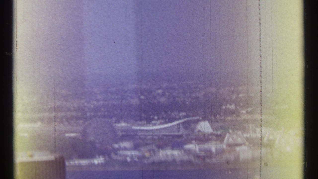 Hazy elevated view of a river, distant buildings, and a bridge through faded 8mm film.