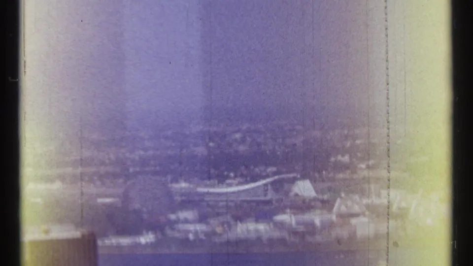 1967 Ottawa home-movie frame with a wide river, distant waterfront buildings, and bridge forms under a purple-blue haze.