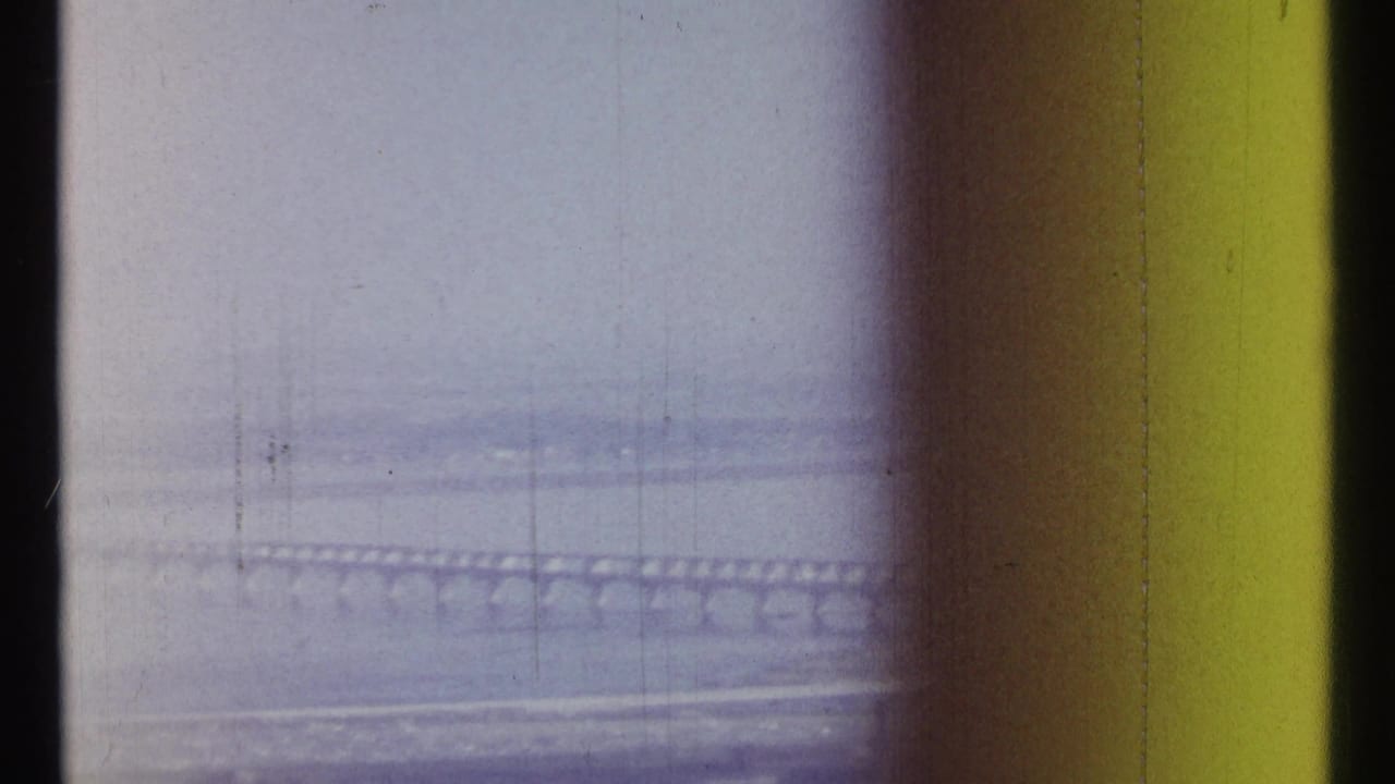 Long bridge crossing water under a hazy sky with dark film borders.