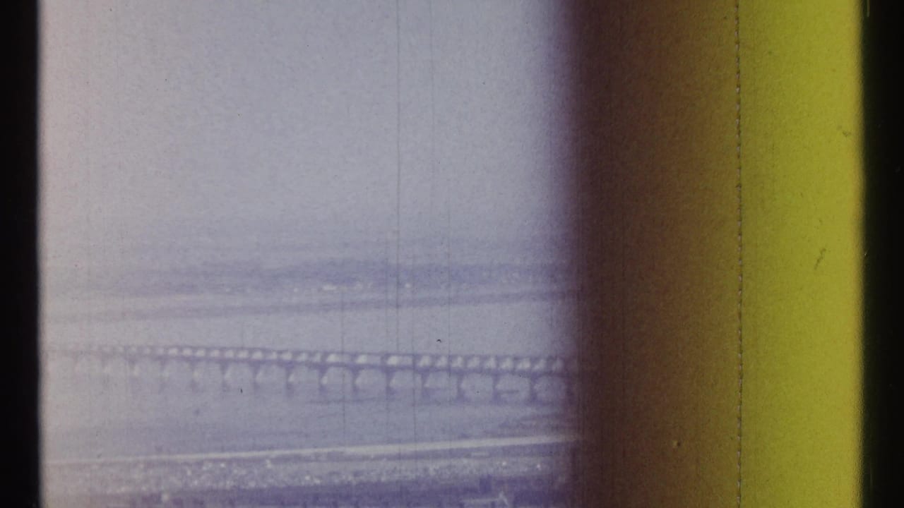 Distant arched bridge over water, framed by dark scan edges and color cast.