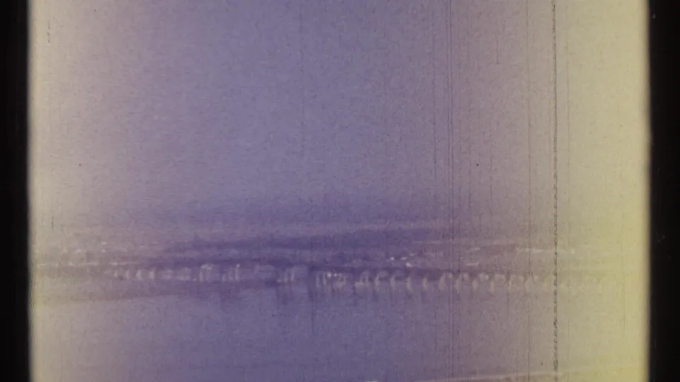 1967 Ottawa aerial home-movie frame showing a wide river, long bridge, and hazy city skyline on faded 8mm film.