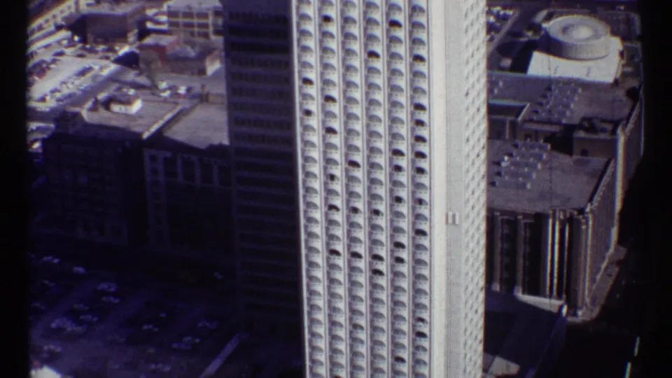 1967 Ottawa aerial frame approaching downtown buildings, centered on a high-rise with a repeated arched window pattern.