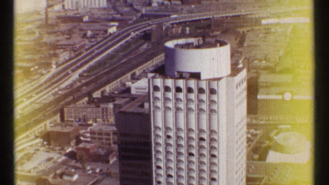 Aerial view of a tall high-rise with arched window bays beside elevated transport lines.