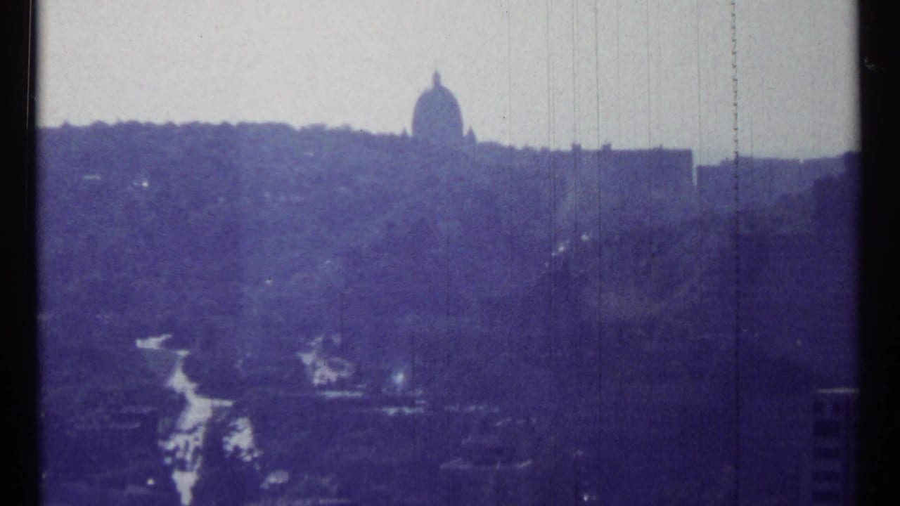 Distant domed building above a wooded ridge with a winding road below.