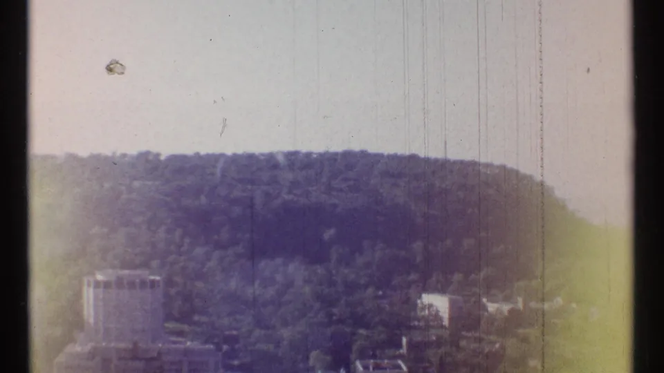 Ottawa home-movie frame from 1967 showing a wooded ridge, scattered buildings, and strong light leak or color fading on 8mm film.