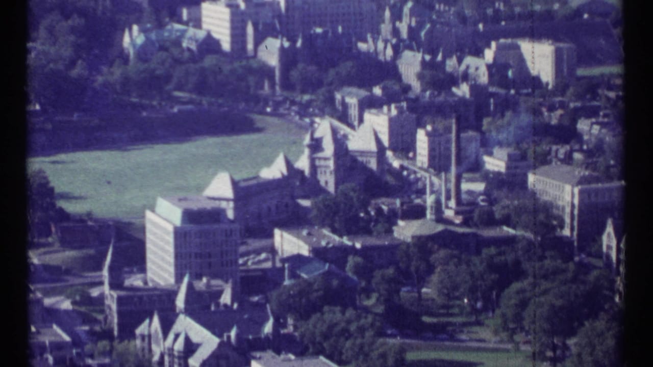 Aerial view over Ottawa buildings, green field, trees, and streets on faded 8mm film.