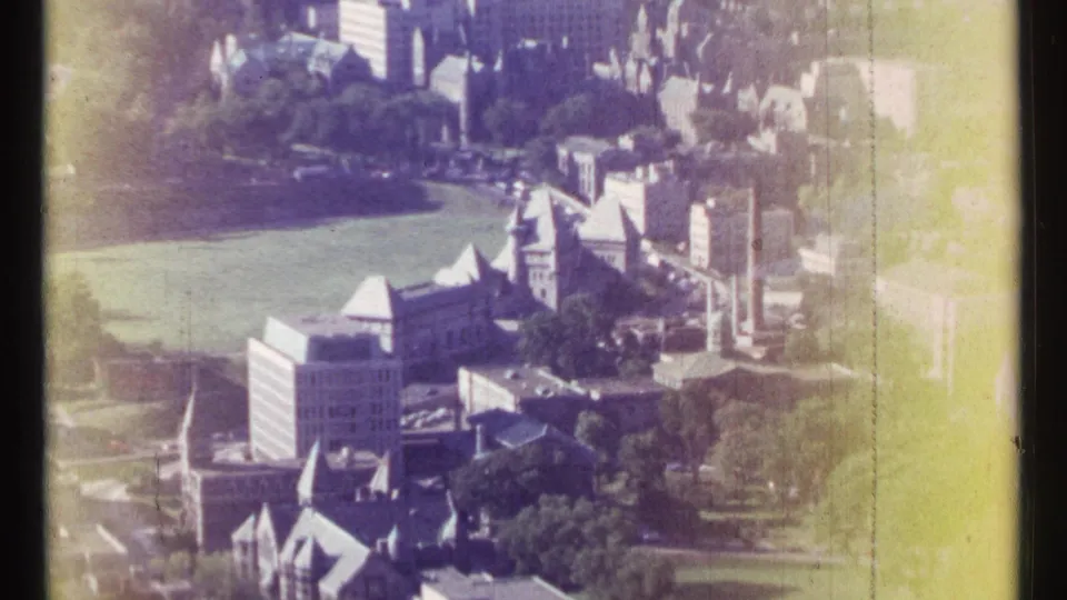 1967 Ottawa aerial view showing dense buildings, green space, roads, tree cover, and strong yellow edge flare from the original 8mm film.