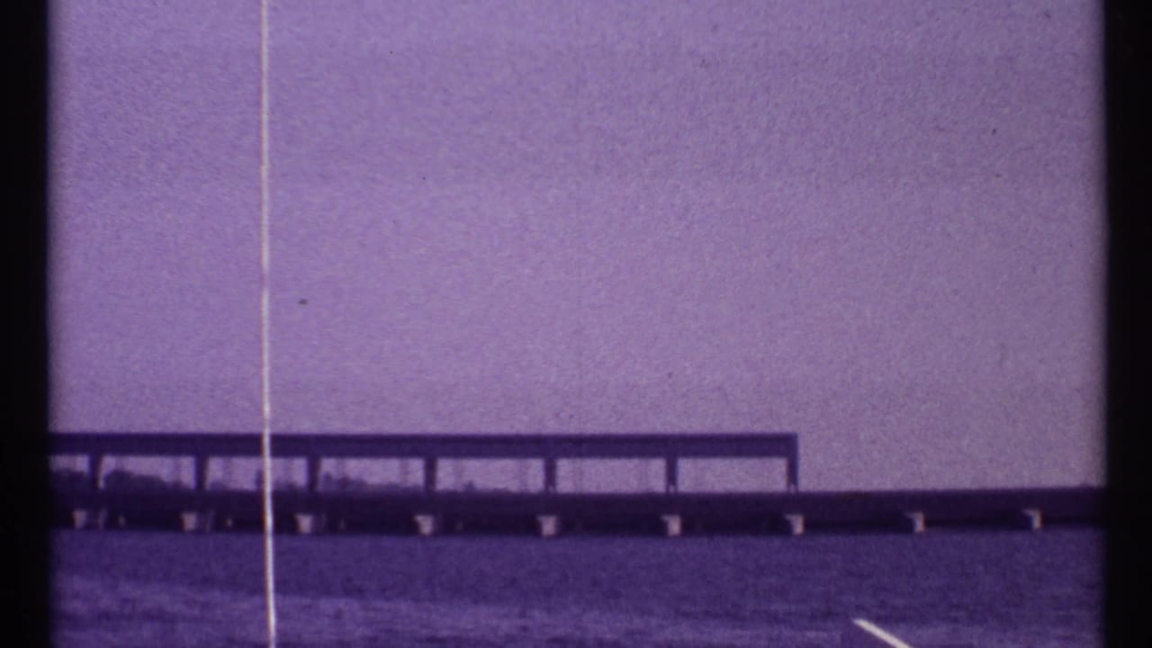 Long low bridge or causeway crossing water beneath a purple-tinted sky.