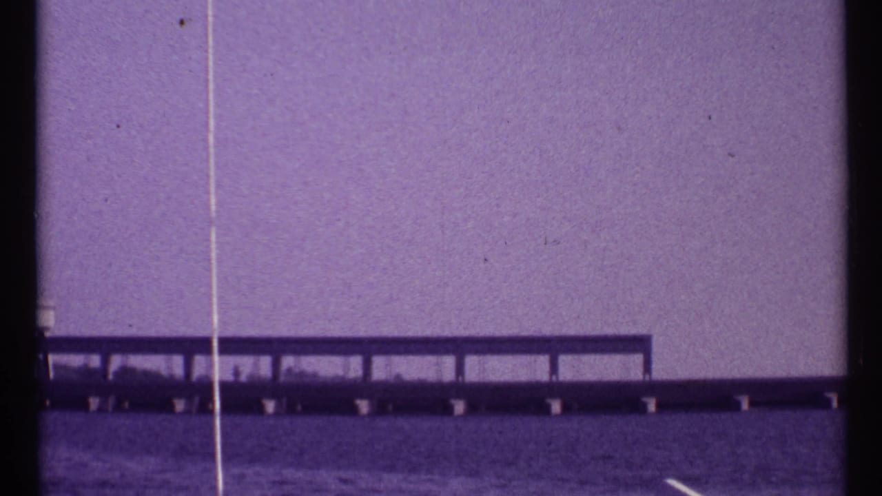 Bridge structure over water with rail-like supports and visible film scratches.