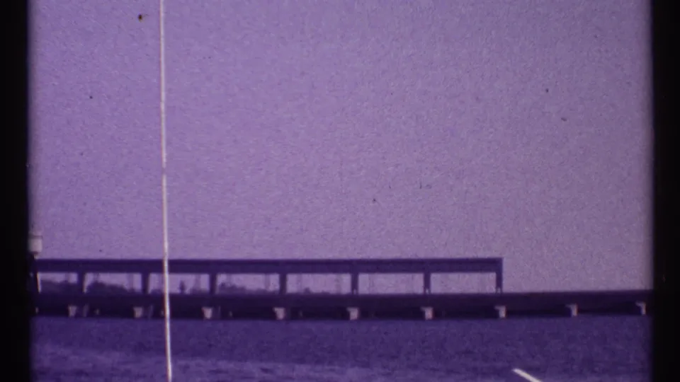 Purple-tinted 8mm view of a low bridge over water in Toronto, with rail-like supports and visible gate edge marks.