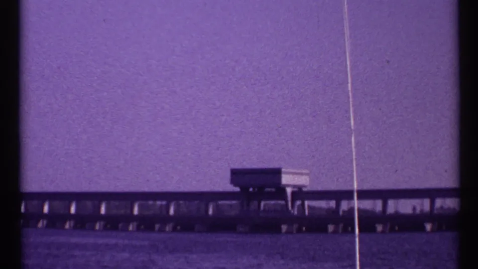 Purple-tinted 8mm home-movie frame of a low Toronto bridge over water with a small bridge building and visible film wear.