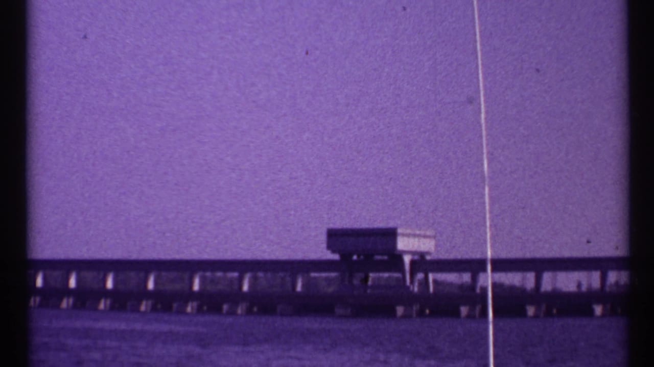 Distant low bridge-like structure across calm water under a purple-tinted sky.