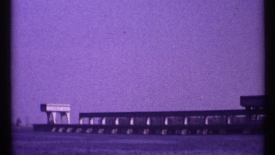 1967 Toronto 8mm view of calm water, a distant low span, and a block-like feature against an open purple sky.