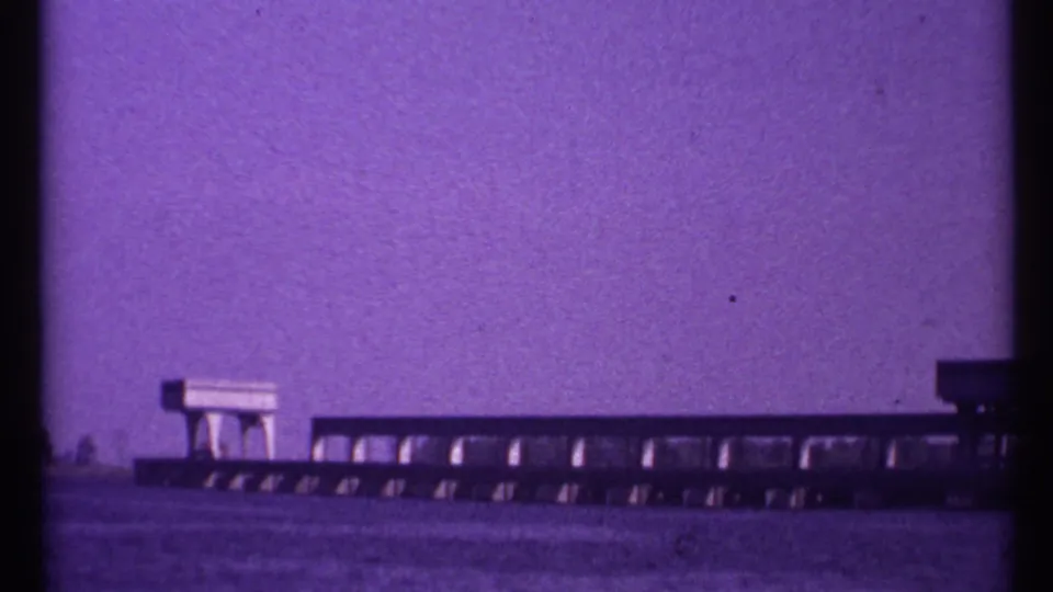 1967 Toronto 8mm frame showing a long low concrete waterway structure with repeating openings and rail-like details.