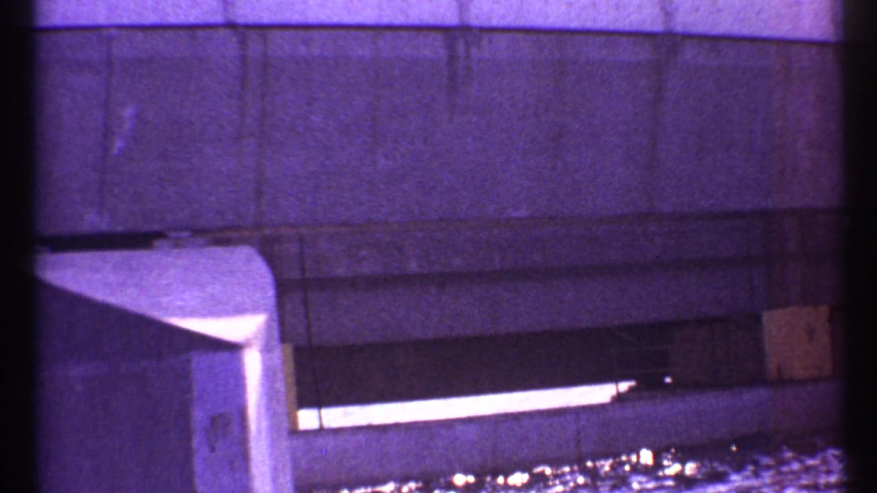 Concrete structure seen close up with a bright horizontal opening and water reflections below.