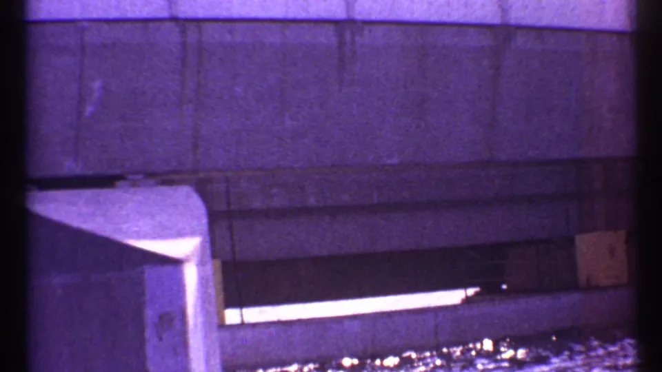 Close 8mm view of the Toronto concrete dam structure, with a bright slit-like opening and reflected water at the lower edge.