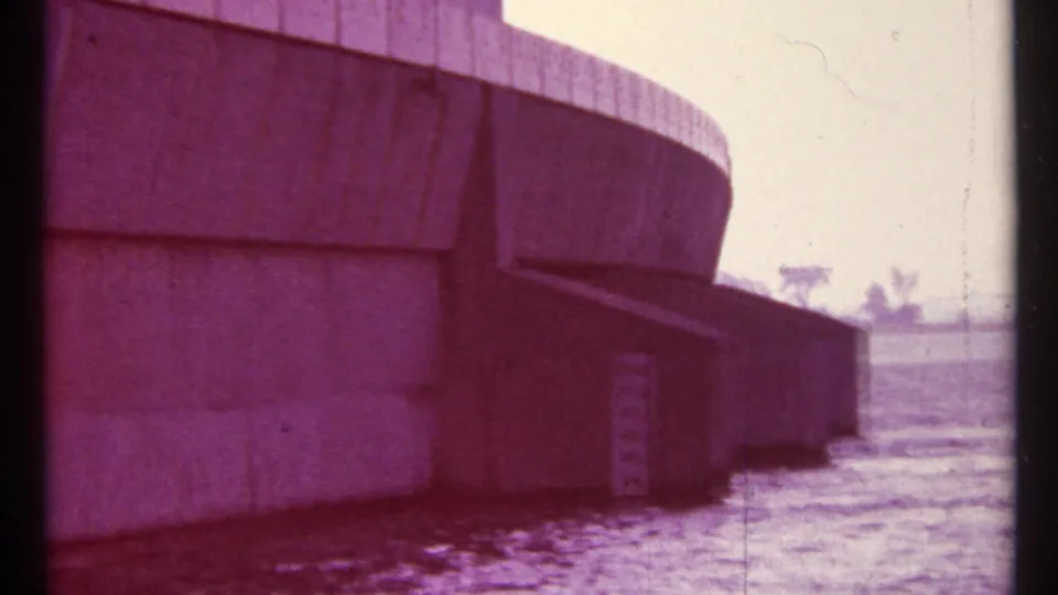 Purple-tinted 8mm frame of the Toronto concrete dam or water-control structure, with water below and a faint shoreline beyond.
