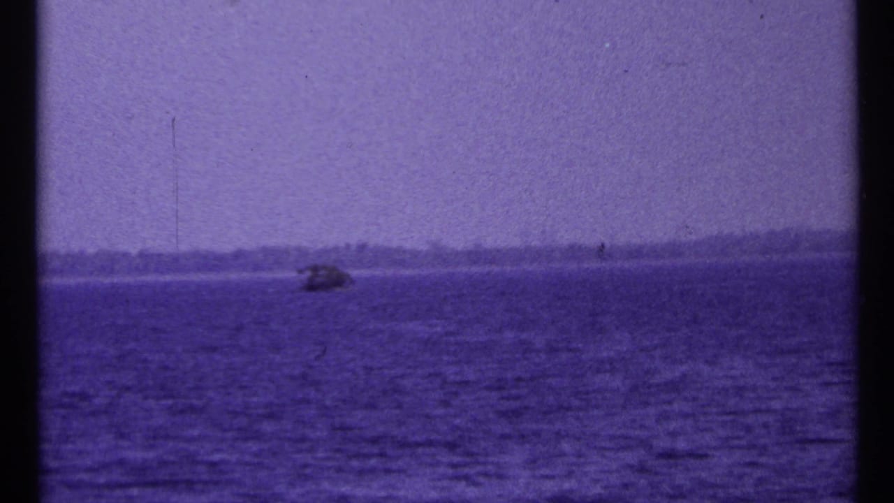 Small boat on open lake water beneath a hazy sky and distant shoreline.