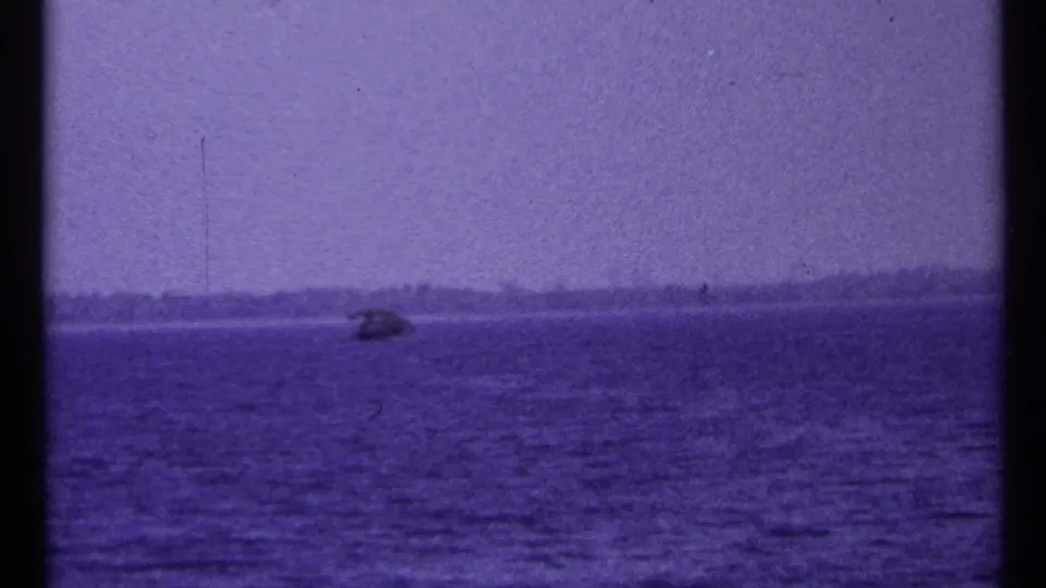1967 Toronto-area 8mm frame showing a small boat far out on a lake with hazy sky, low shoreline, and purple film cast.