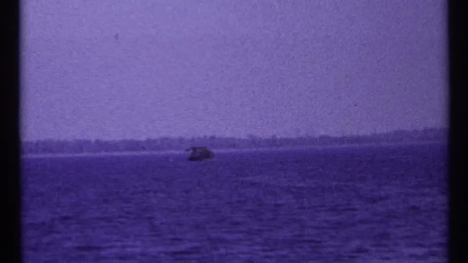 1967 Toronto-area lake view with a small boat near the distant shore, seen through grainy purple-tinted 8mm film.