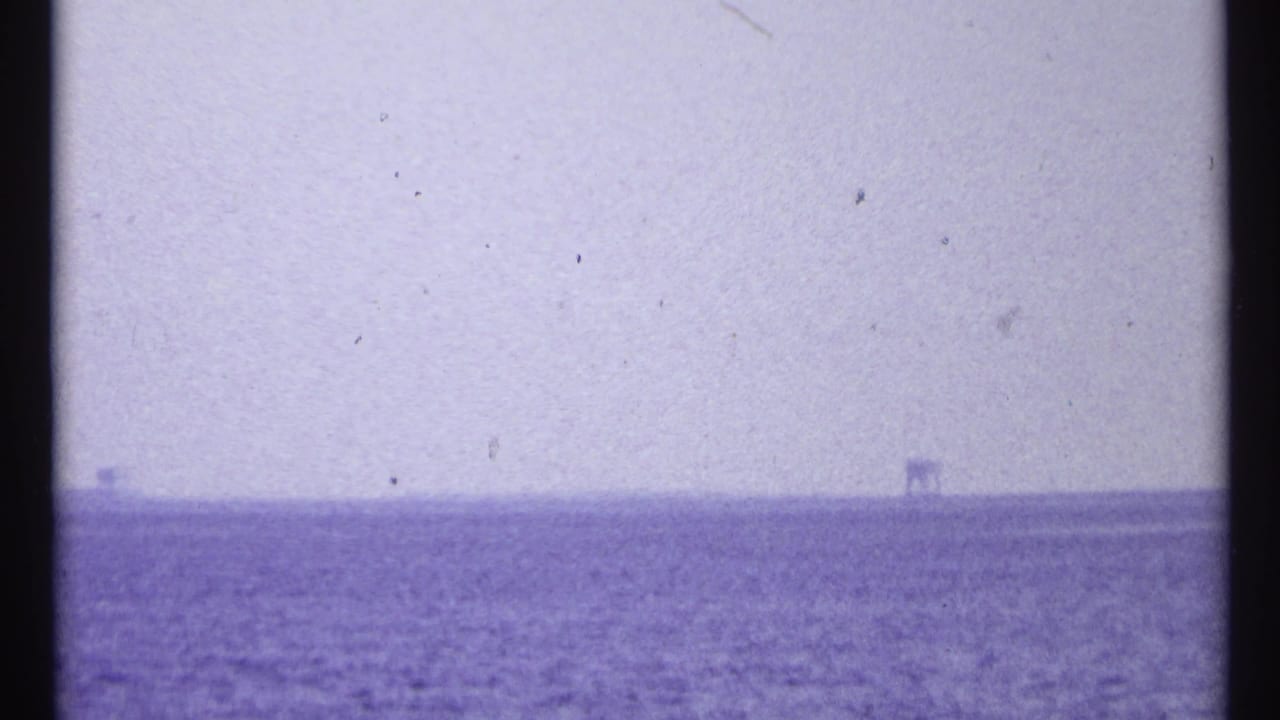 Hazy open water with small distant structures on the horizon.