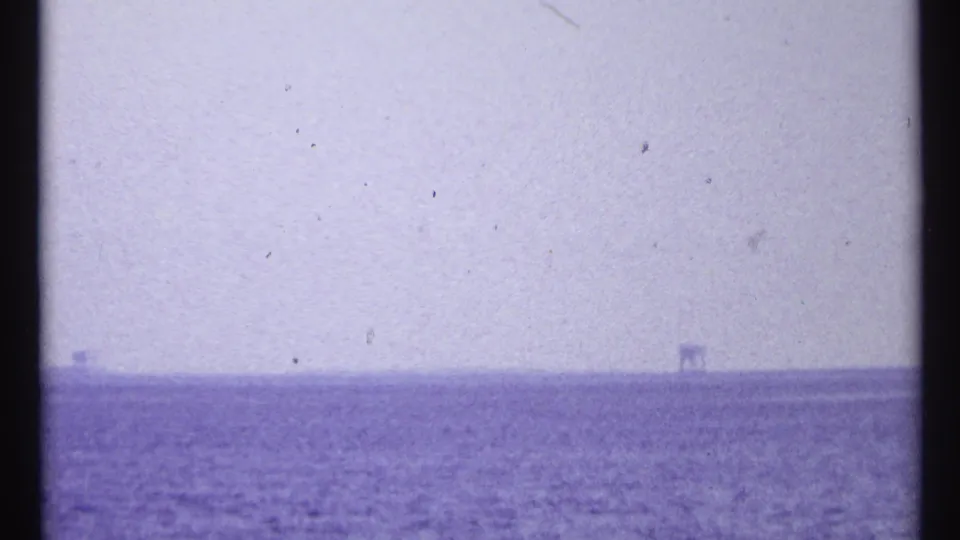 1967 Toronto home-movie frame showing hazy open water and faint structures along a distant horizon.